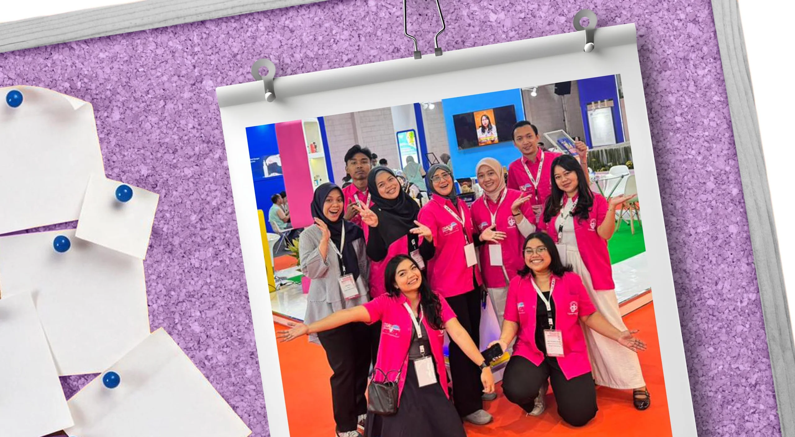 Group of smiling people in pink uniforms posing for a group photo at a trade show/expo.